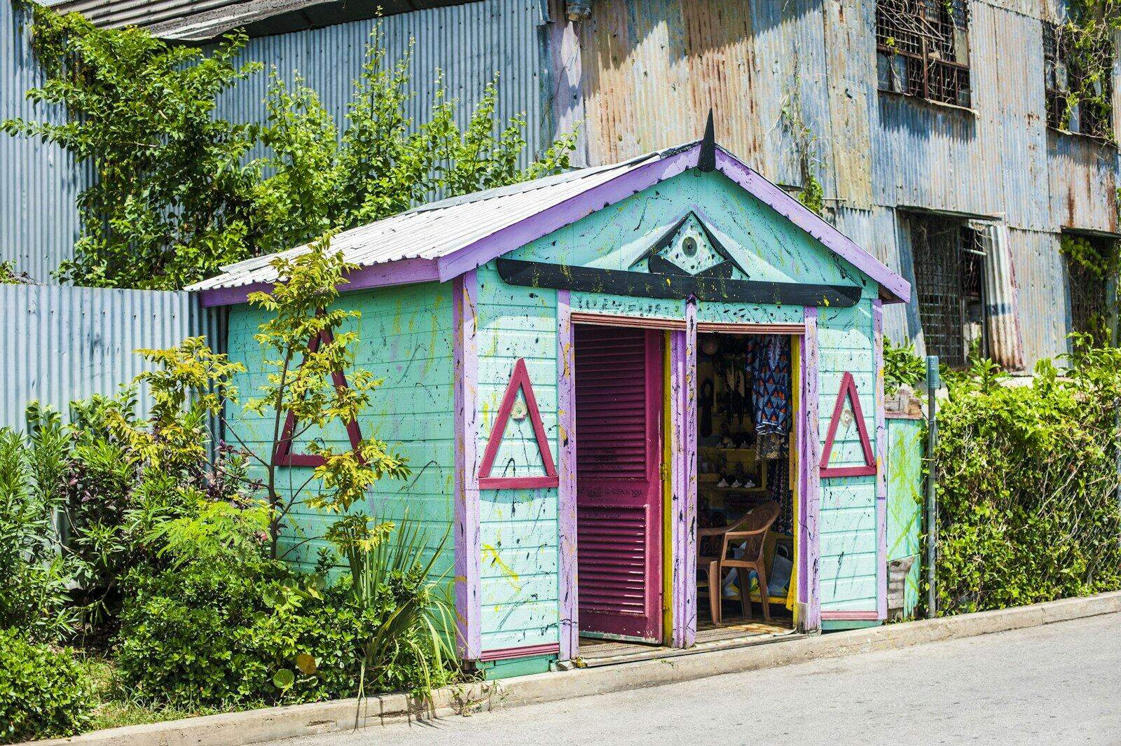 Small turquoise wooden craft shop with purple trim and an open door beside a corrugated metal wall in Bridgetown, Barbados